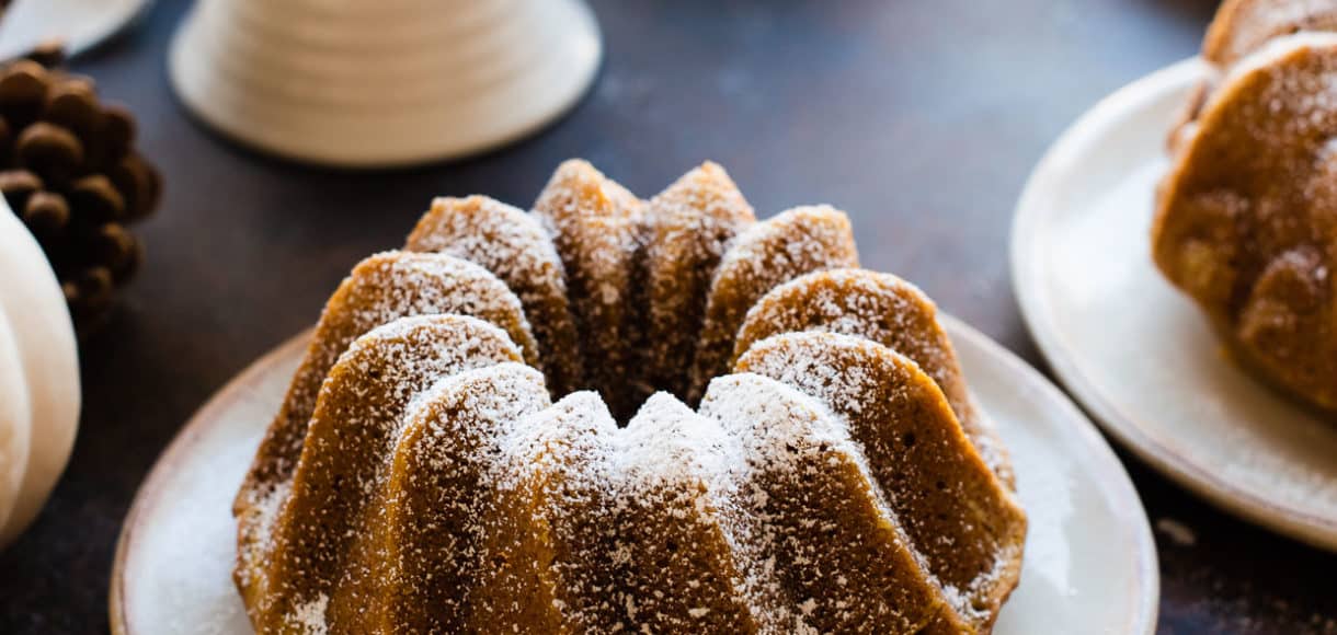 Pumpkin Spice Bundt Cakes sprinkled with powdered sugar. White pumpkins and pine cones in background.