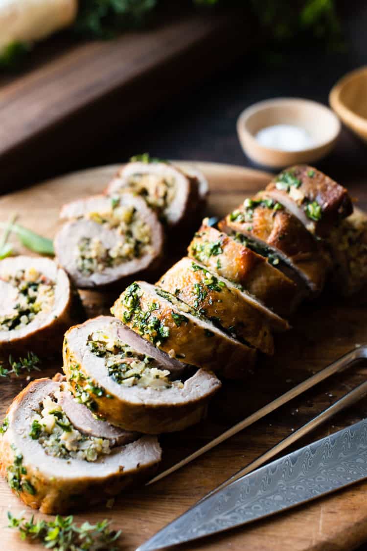 Quinoa Stuffed Pork Tenderloin sliced on a wooden cutting board garnished with fresh herbs.