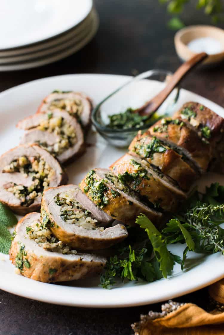 Quinoa Stuffed Pork Tenderloin sliced on a platter garnished with fresh herbs.