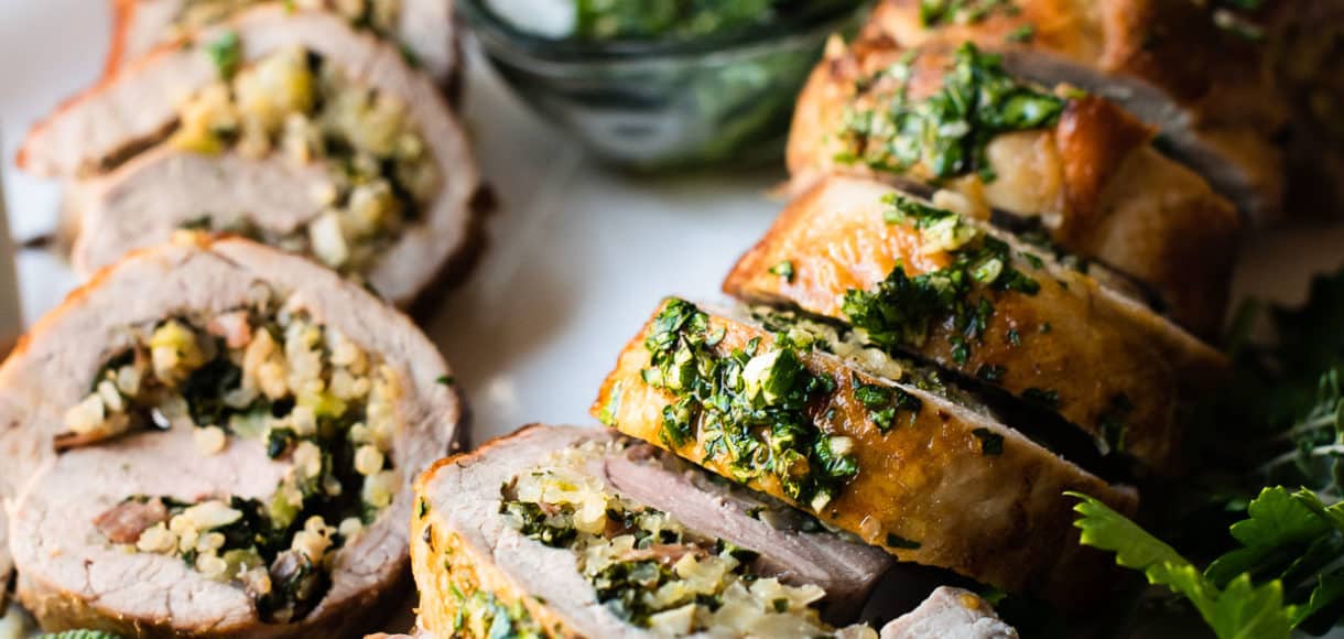 Quinoa Stuffed Pork Tenderloin sliced on a platter garnished with fresh herbs.