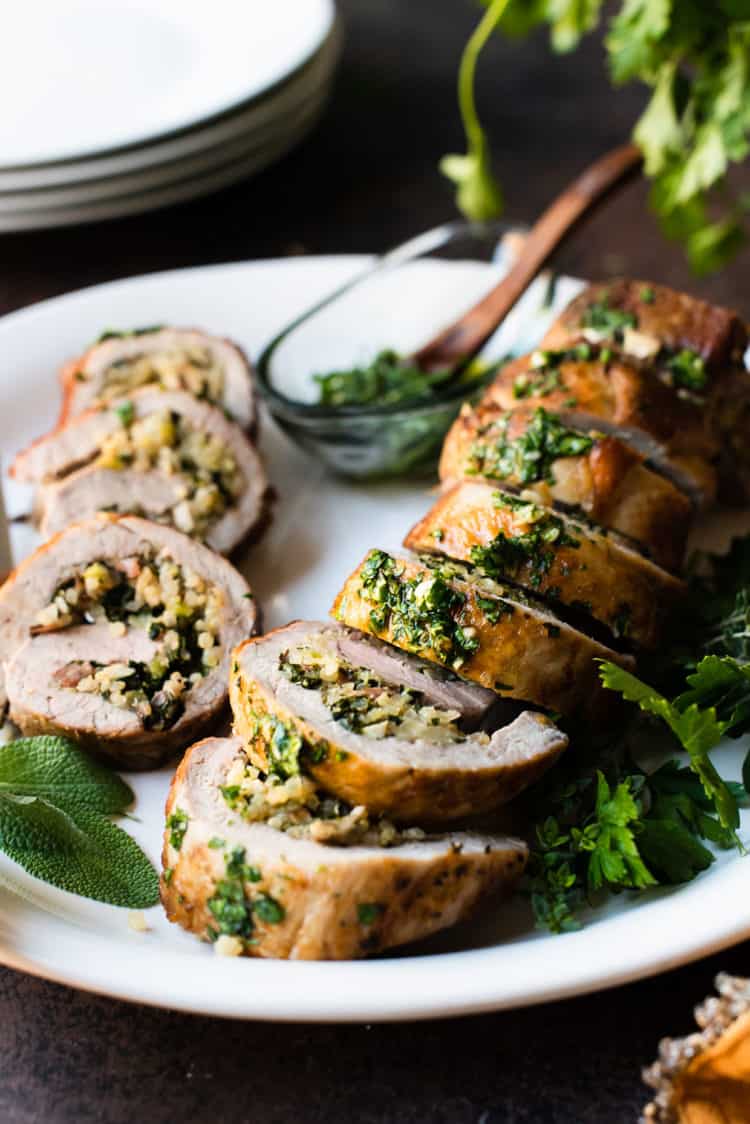 Quinoa Stuffed Pork Tenderloin sliced on a platter garnished with fresh herbs.