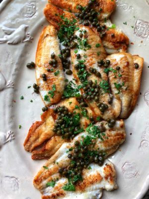 Sole Meunière topped with capers and parsley on a serving platter.