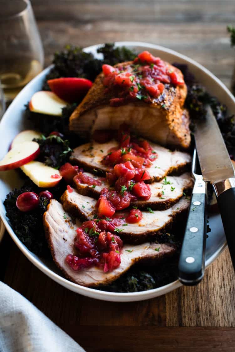 Roast Pork Loin with Apple Chutney sliced on a platter with carving knife on the side.