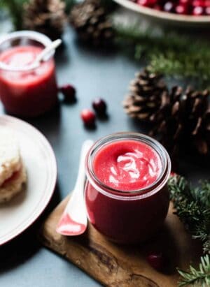 Jar of cranberry curd on a wooden board with pine cones and Christmas greens.
