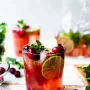 Cranberry Pomegranate Mojito in a glass garnished with limes, cranberries, pomegranate arils and mint.