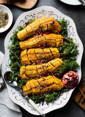 Maple Cinnamon Hasselback Delicata Squash on a bed of kale salad with pomegranates and pecans.