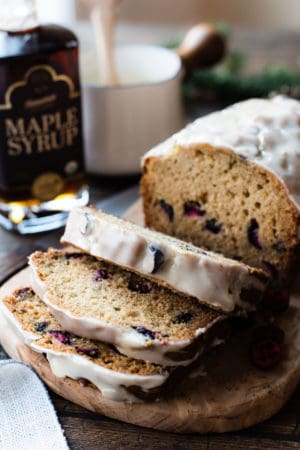 Maple-Glazed Cranberry Bread sliced on a cutting board with maple syrup in the background.