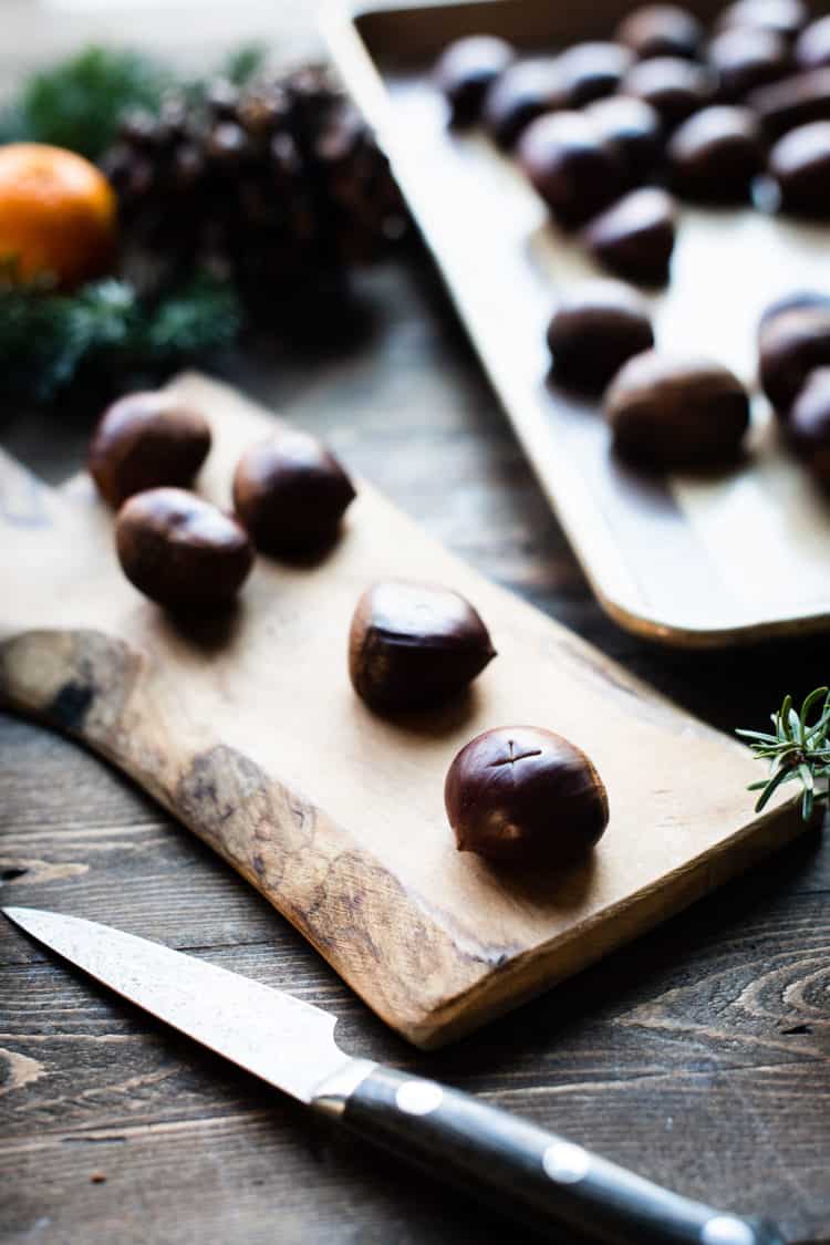 Scoring oven roasted chestnuts with a knife on a wood board.