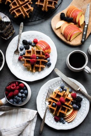 Apple Oatmeal Blender Waffles topped with fresh berries, slices of apple on white plates.