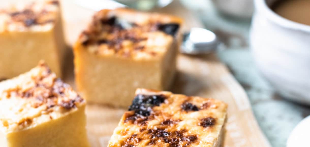 Slices of Cassava Cake on a board with coffee in the background.