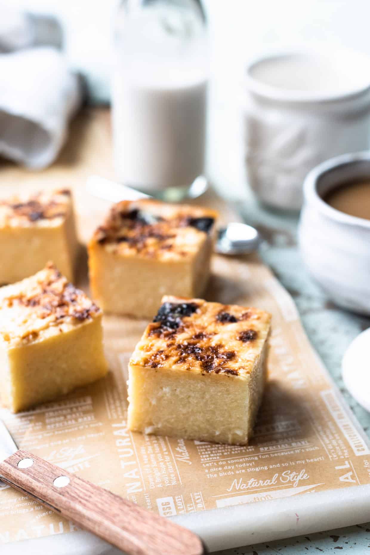 Slices of Cassava Cake on a board with coffee in the background.