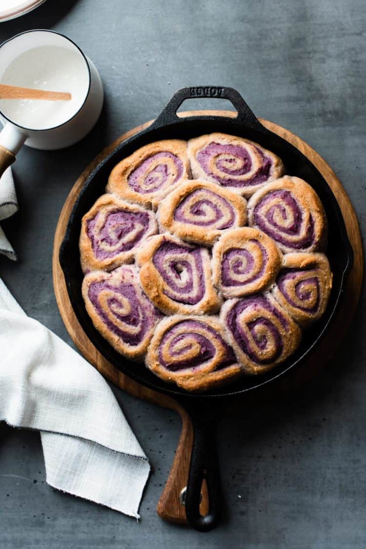 Vegan Coconut Ube Rolls in a cast iron skillet with coconut glaze on the side.