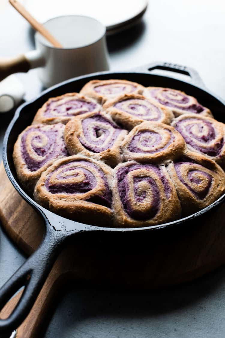 Coconut Ube Rolls in a cast iron skillet on a wooden cutting board before it is glazed.