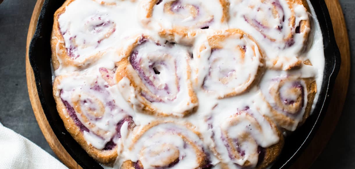 Vegan Coconut Ube Rolls in a cast iron skillet covered with coconut glaze.