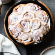 Vegan Coconut Ube Rolls in a cast iron skillet covered with coconut glaze.