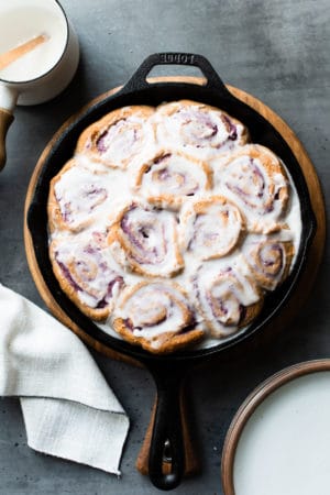 Vegan Coconut Ube Rolls in a cast iron skillet covered with coconut glaze.