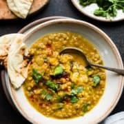 Bowl of Curried Butternut Squash Lentil Soup with naan bread, garnished cilantro and chili oil.