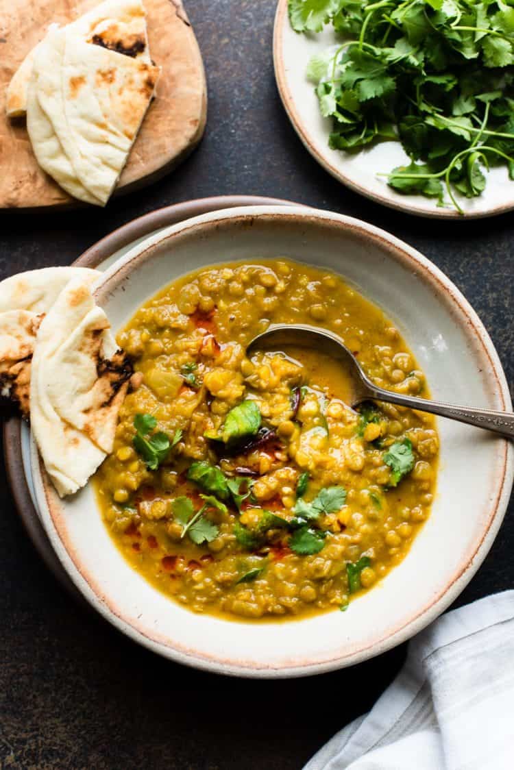 Bowl of Curried Butternut Squash Lentil Soup with naan bread, garnished cilantro and chili oil.