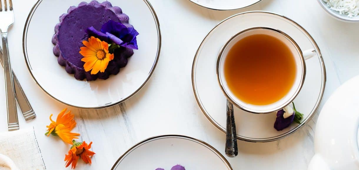 Ube Halaya served with edible flowers on white plates and served with tea.