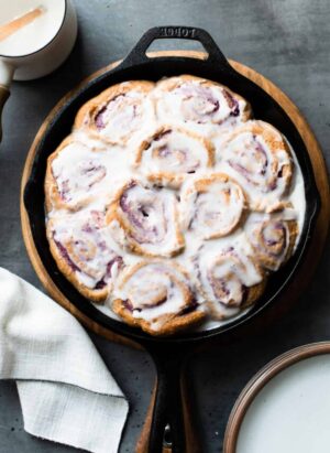 Vegan Coconut Ube Rolls in a cast iron skillet covered with coconut glaze.