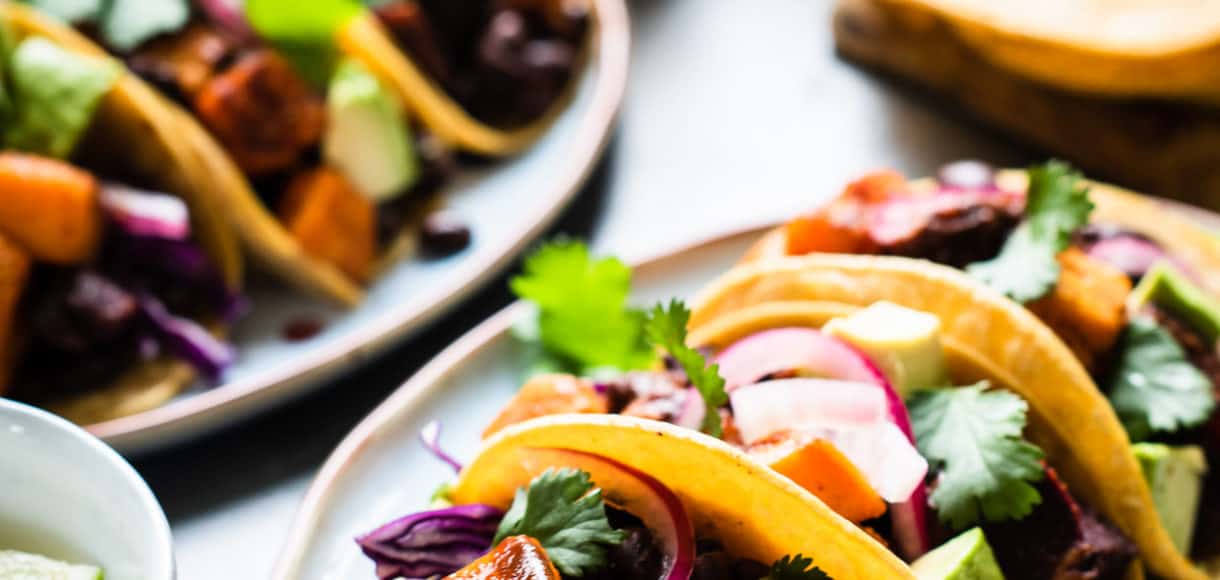 Chipotle-Spiced Sweet Potato Tacos garnished with red cabbage, cilantro and chipotle salsa on a platter.