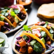 Chipotle-Spiced Sweet Potato Tacos garnished with red cabbage, cilantro and chipotle salsa on a platter.
