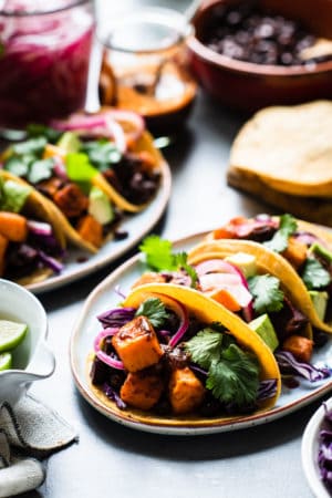 Chipotle-Spiced Sweet Potato Tacos garnished with red cabbage, cilantro and chipotle salsa on a platter.