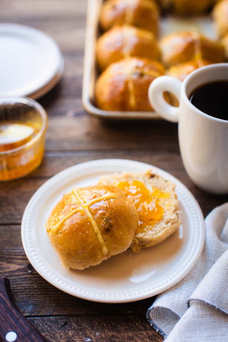 Hot cross bun with jam on a plate and served with coffee.