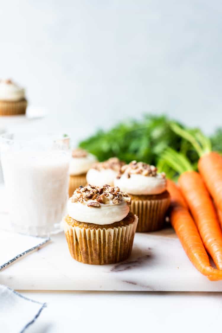 Vegan carrot cake muffins with cream cheese frosting topped with pecans and served with a glass of almond milk.