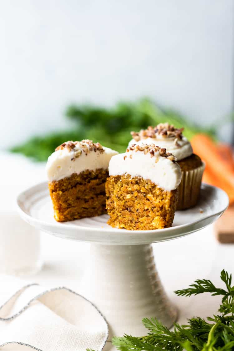 Carrot cake cupcakes with cream cheese frosting sliced in half on a cake stand.