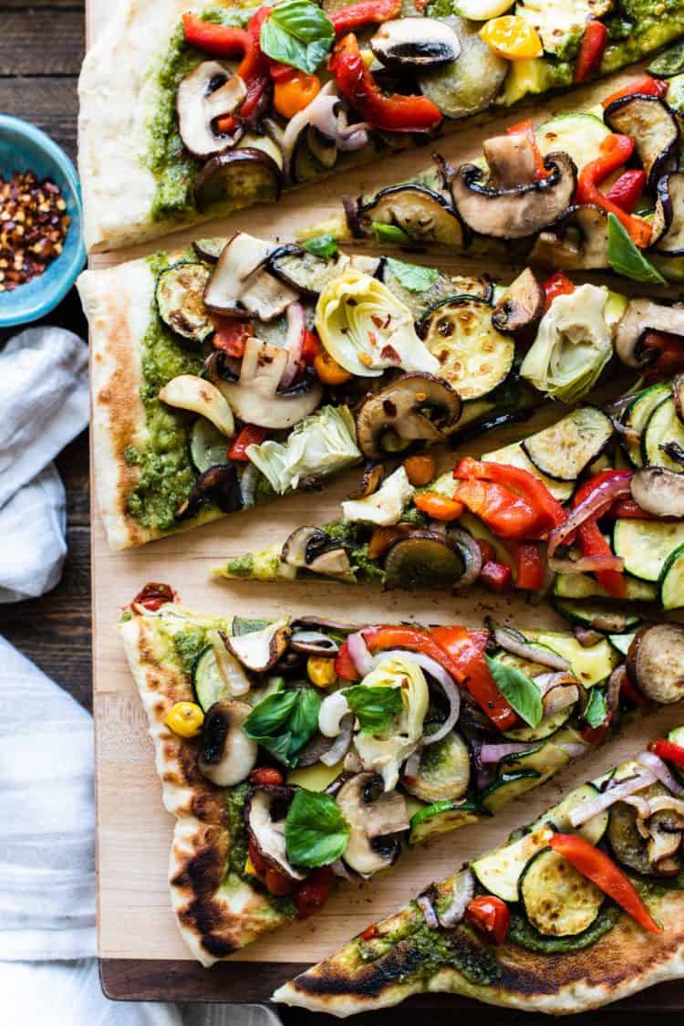Slices of grilled vegetable pizza on a wooden cutting board.