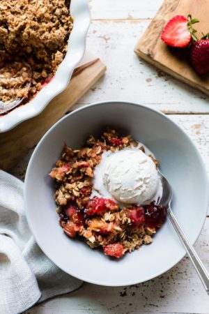 Strawberry Rhubarb Crisp in a light gray bowl with a scoop of ice cream.