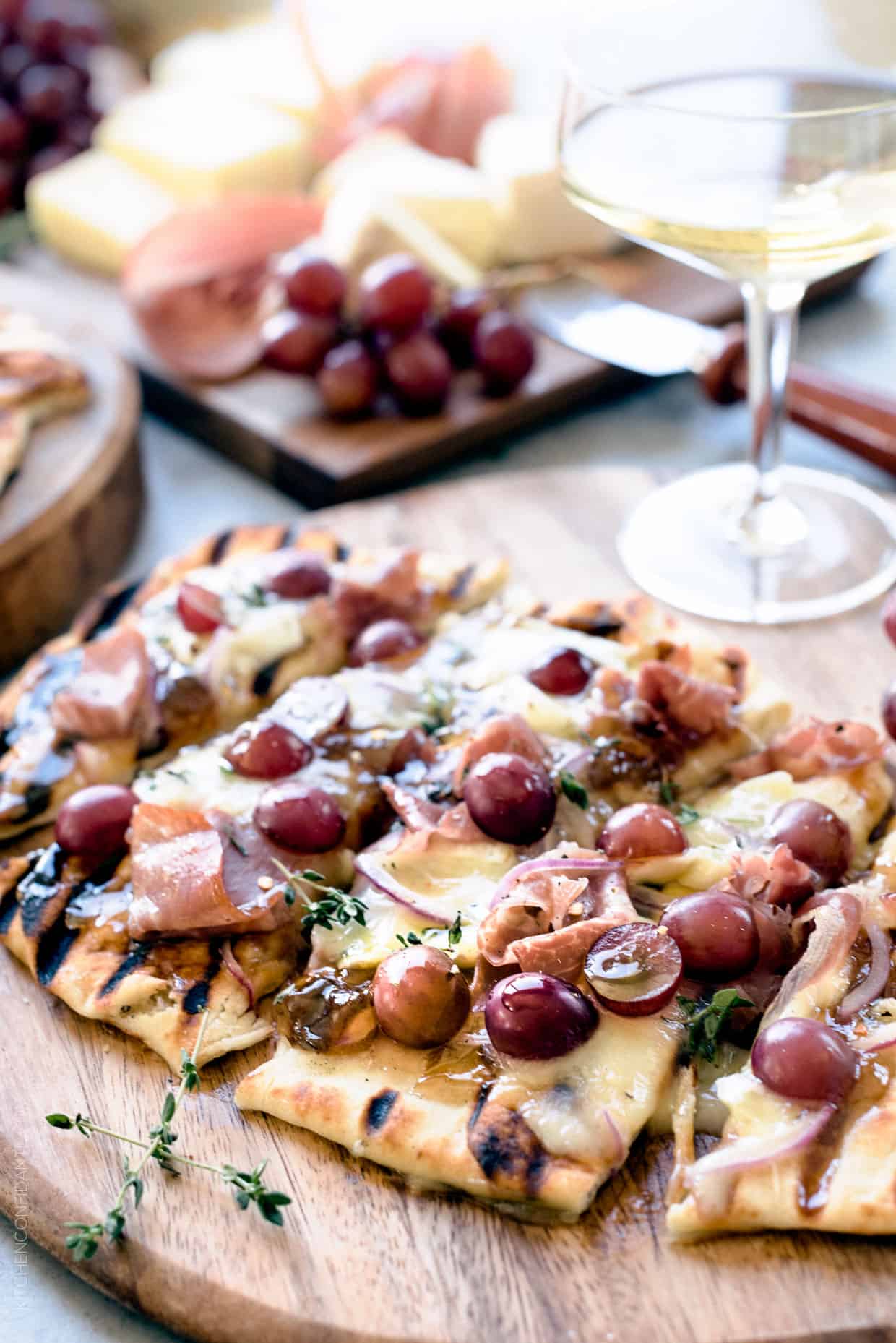 Grilled Naan Flatbread with Grapes, Onion Jam, Prosciutto and Double-Crème Cheese on a wooden serving board.