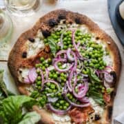 Ricotta Pizza with Prosciutto topped with Fresh Pea Salad on parchment paper.