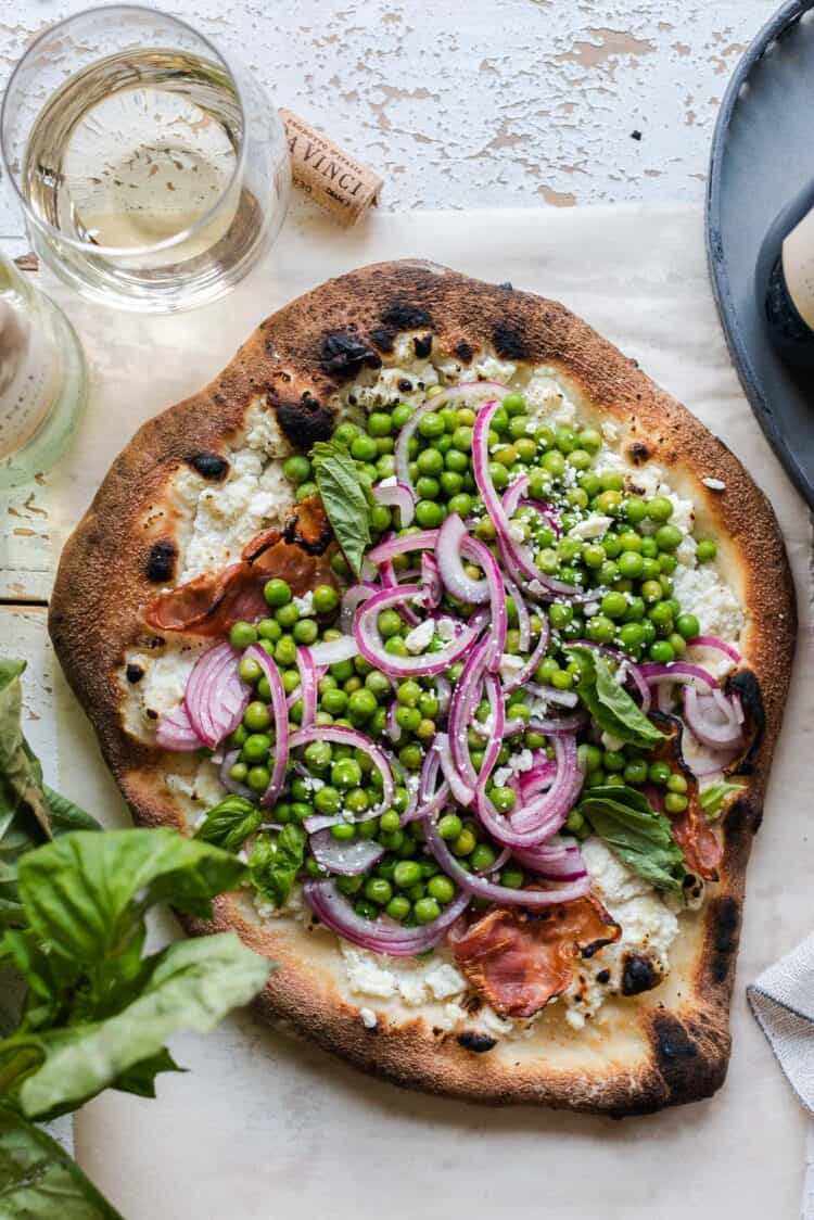 Ricotta Pizza with Prosciutto topped with Fresh Pea Salad on parchment paper.