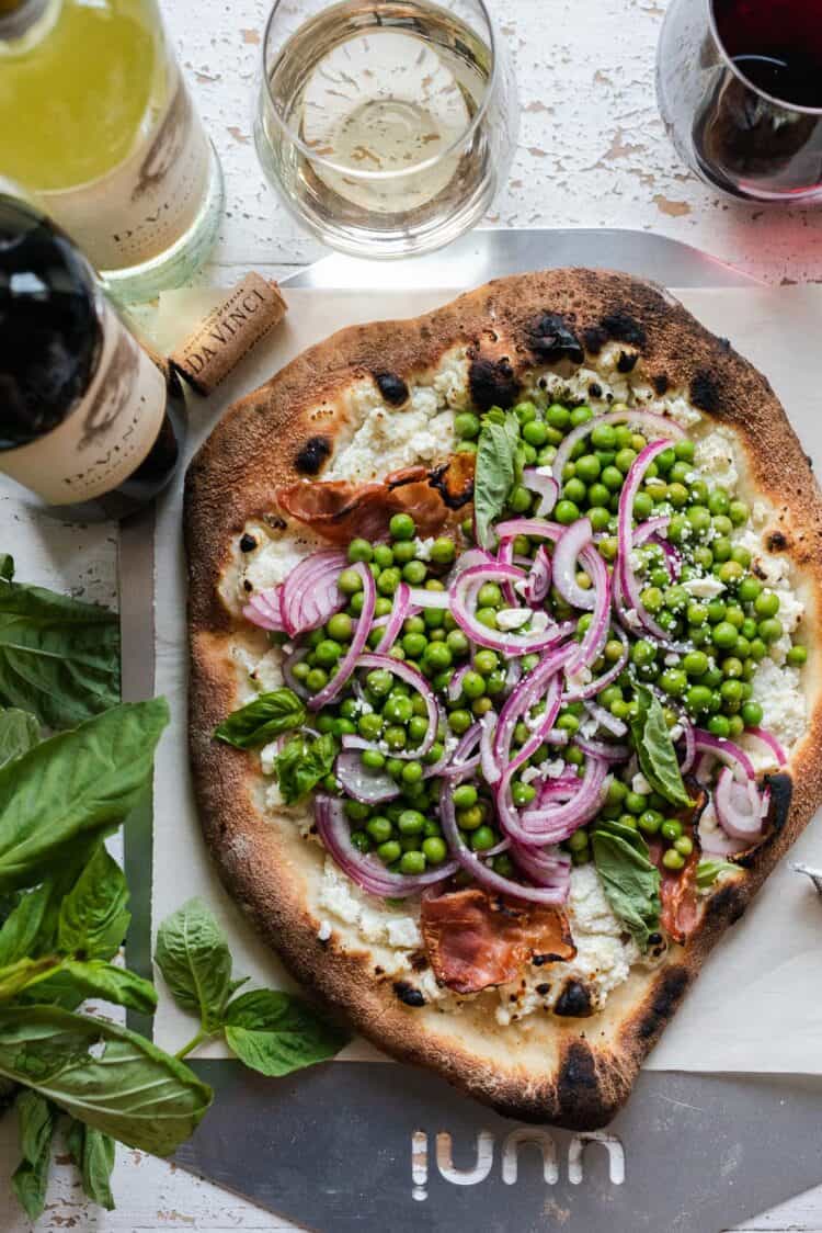 Ricotta Pizza with Prosciutto topped with Fresh Pea Salad on parchment paper.