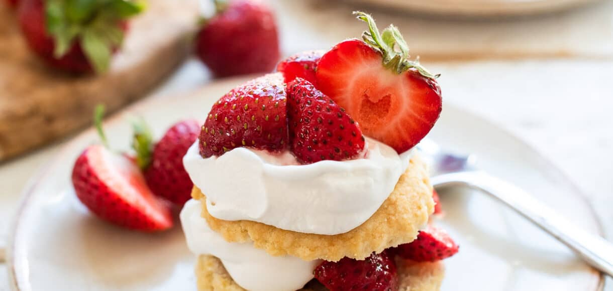 Vegan strawberry shortcake with layers of biscuit, strawberries and coconut whipped cream on a cream colored plate.