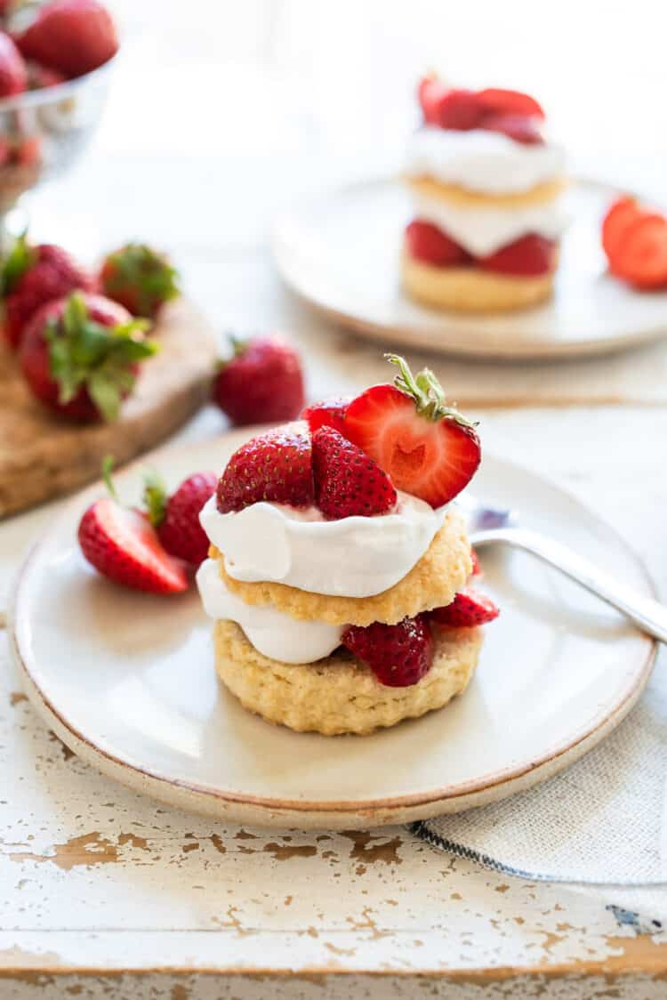 Vegan strawberry shortcake with layers of biscuit, strawberries and coconut whipped cream on a cream colored plate.