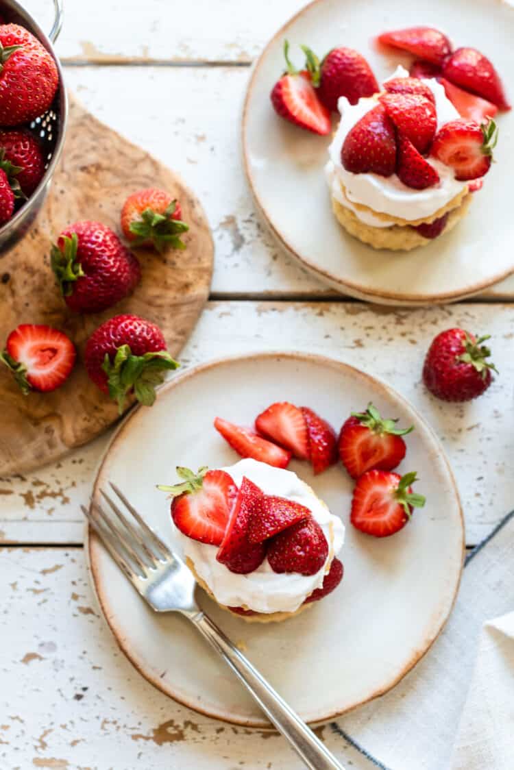 Vegan strawberry shortcake with layers of biscuit, strawberries and coconut whipped cream on a cream colored plate.