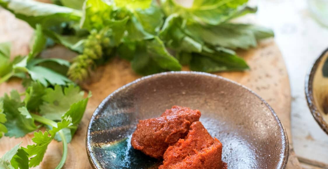 Red curry paste in a bowl with garlic and fresh basil.