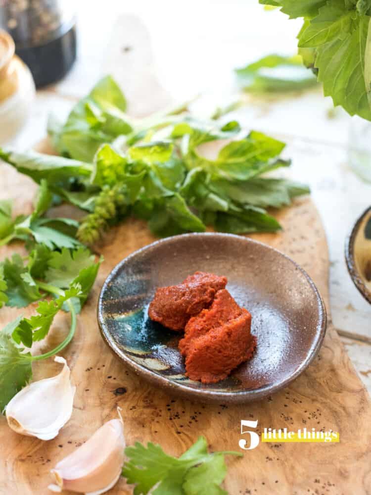 Red curry paste in a bowl with garlic and fresh basil.