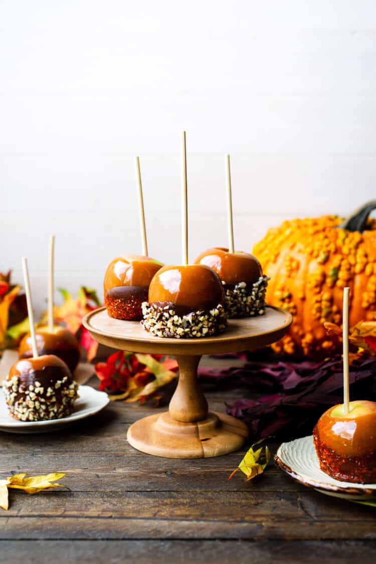 Double Dipped Chocolate Caramel Apples on a cake stand surrounded with pumpkins.