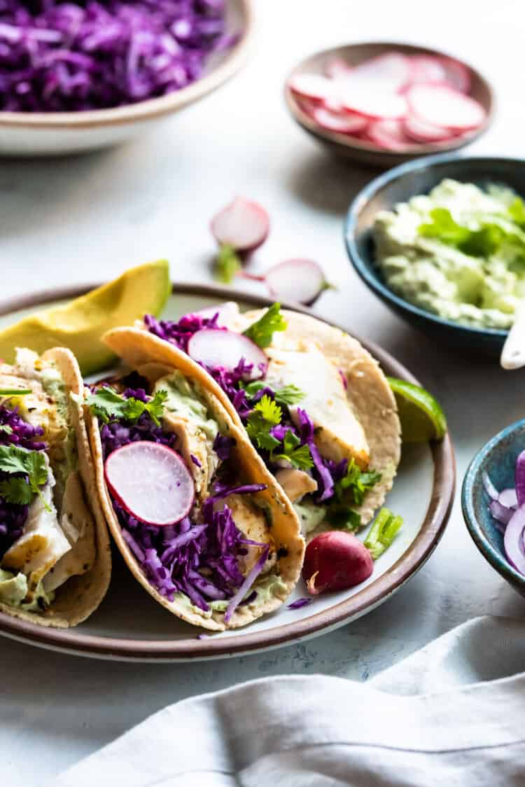 Grilled Fish Tacos with Avocado-Cilantro Sauce on a plate garnished with red cabbage, radishes and jalapeño.