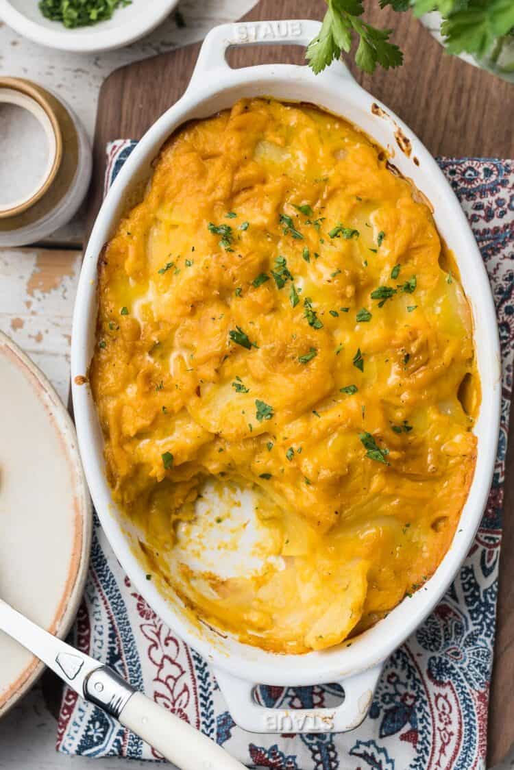 Butternut Squash Scalloped Potatoes in a white oval baking dish on a board.