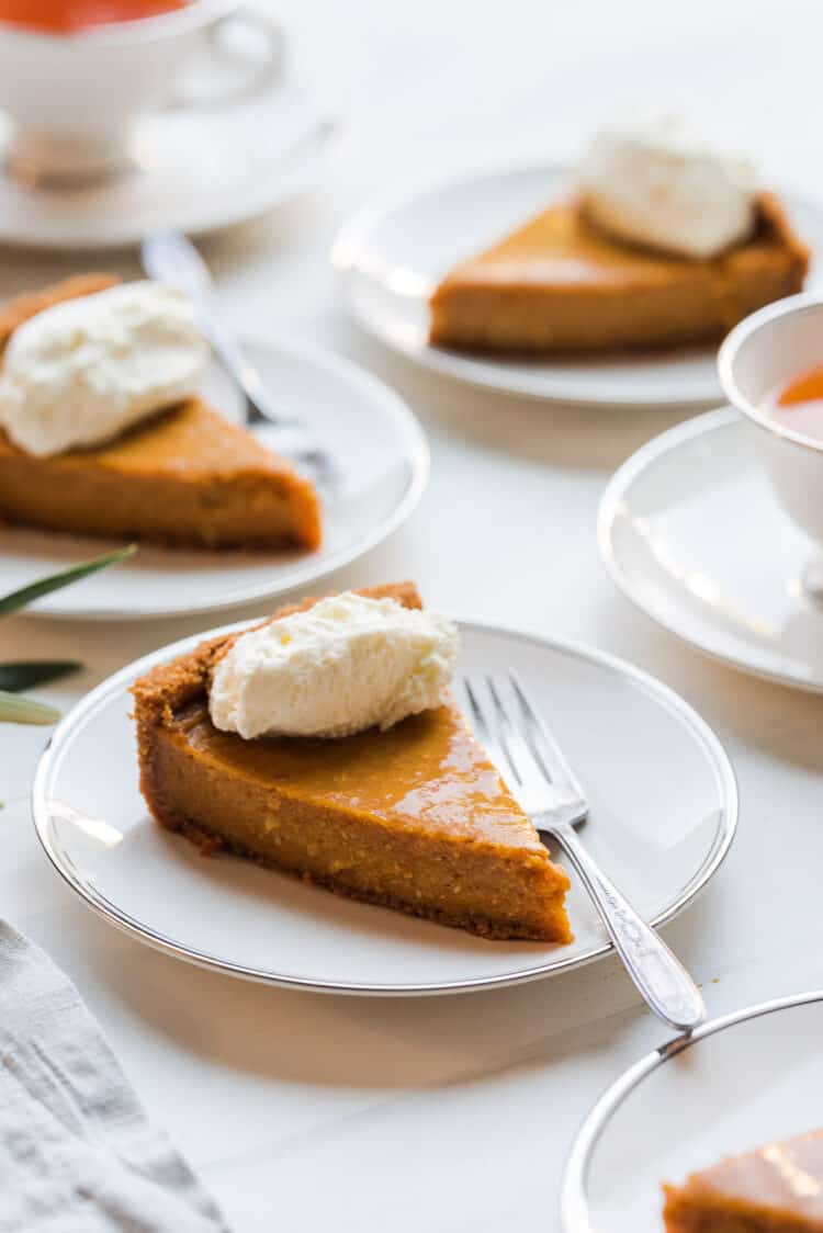 Slices of Cassava Pumpkin Pie and whipped cream on white plates with cups of tea.