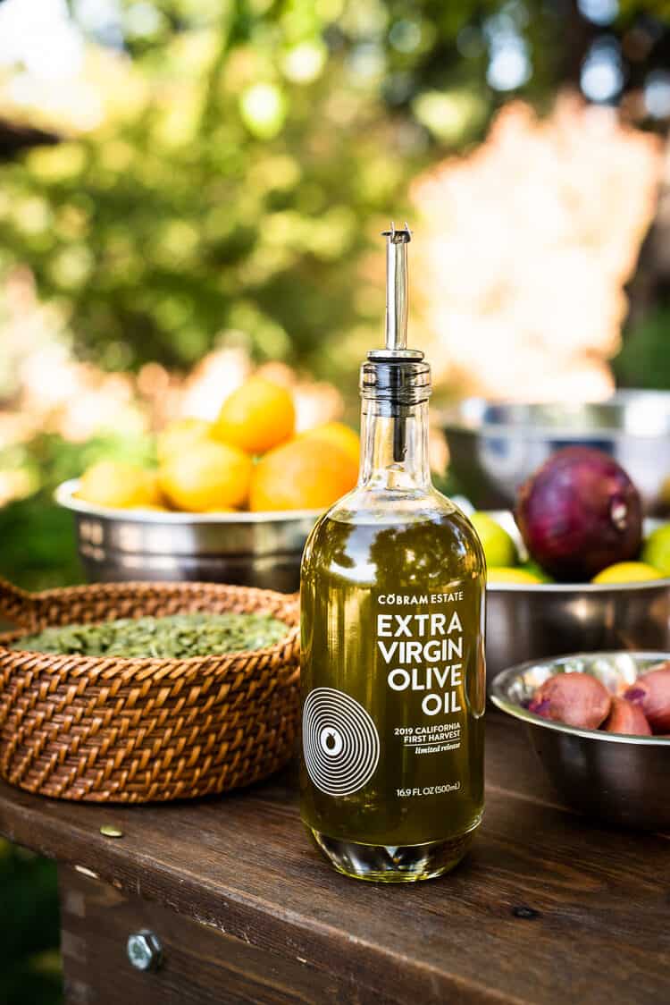 First harvest olive oil from Cobram Estate on a wooden table with ingredients.