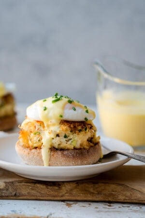 Crab Cake Benedict: Dungeness crab cake with poached egg and easy hollandaise sauce on an english muffin on a white plate.