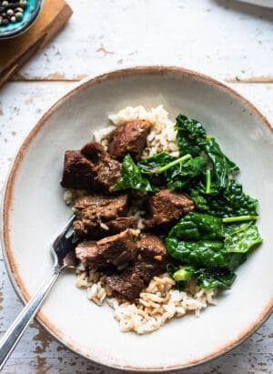 Filipino Pork Adobo served over rice with a side of sautéed kale in a bowl.