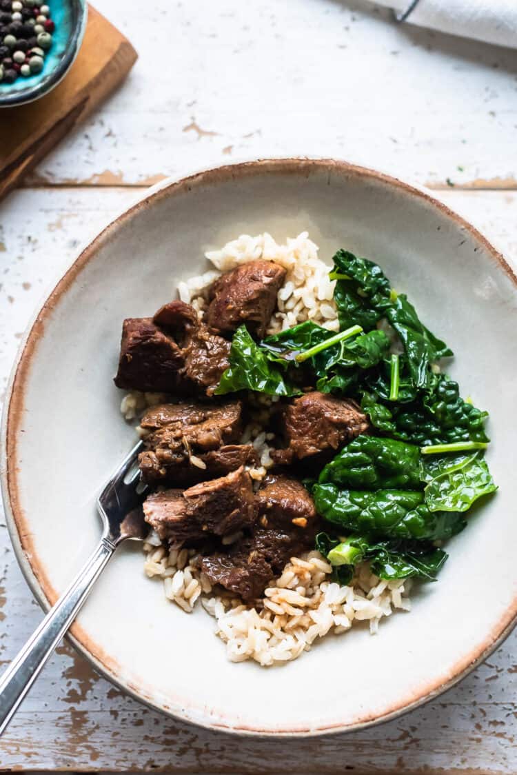 Filipino Pork Adobo served over rice with a side of sautéed kale in a bowl.