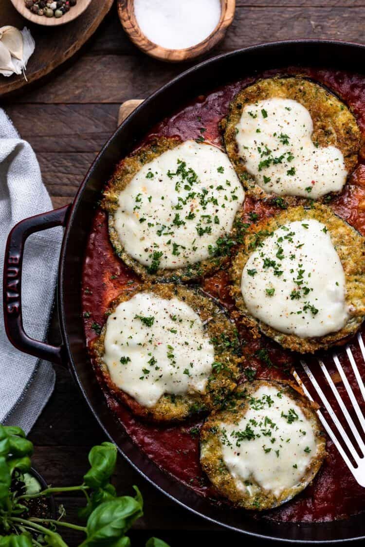 Quinoa Crusted Eggplant Parmigiana in a large dish, topped with mozzarella cheese in a large baking dish on a wooden table.